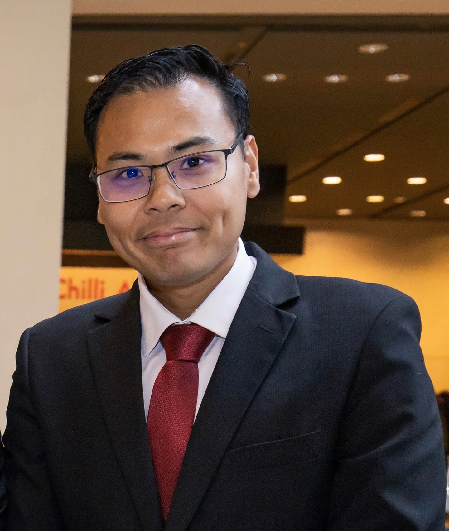 Man in suit and glasses, red tie, "Chilli" sign visible.